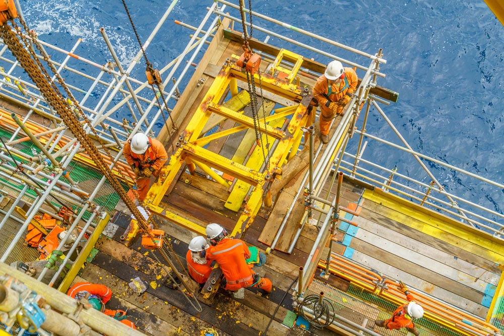 Offshore workers with full personal protective equipment (ppe) performing maintenance and installation new structures at the edge of oil and gas platform.