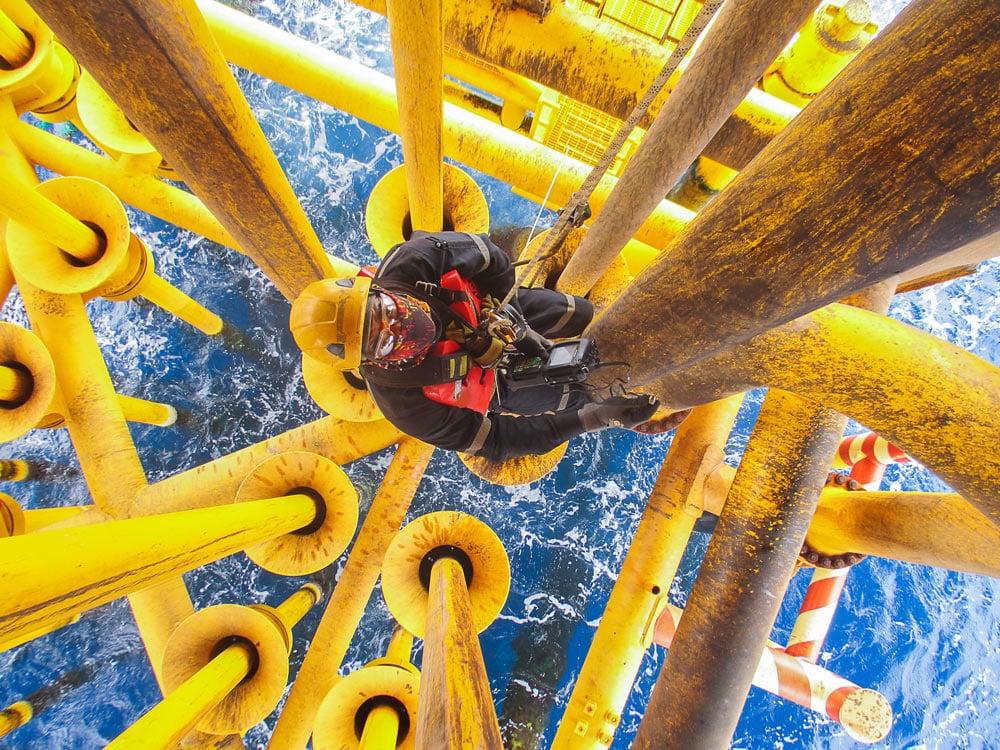 Male worker rope access inspection of thickness offshore drill yellow oil and gas production petroleum pipeline.