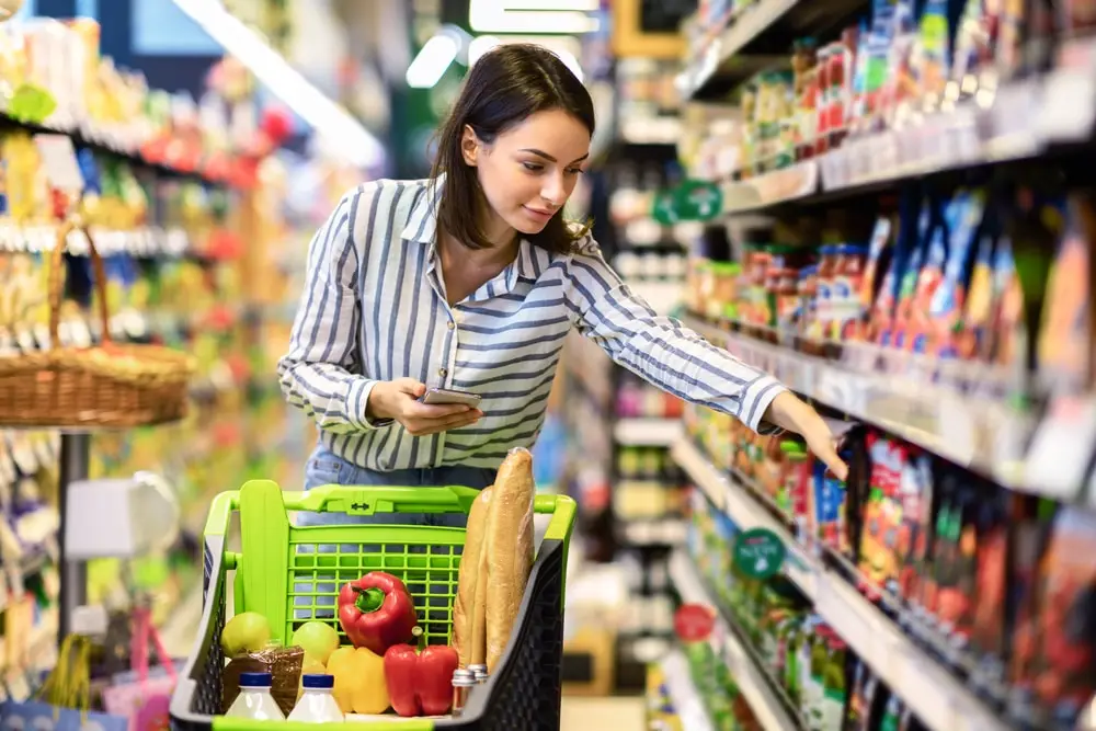 Portrait of millennial lady holding and using smartphone buying food groceries