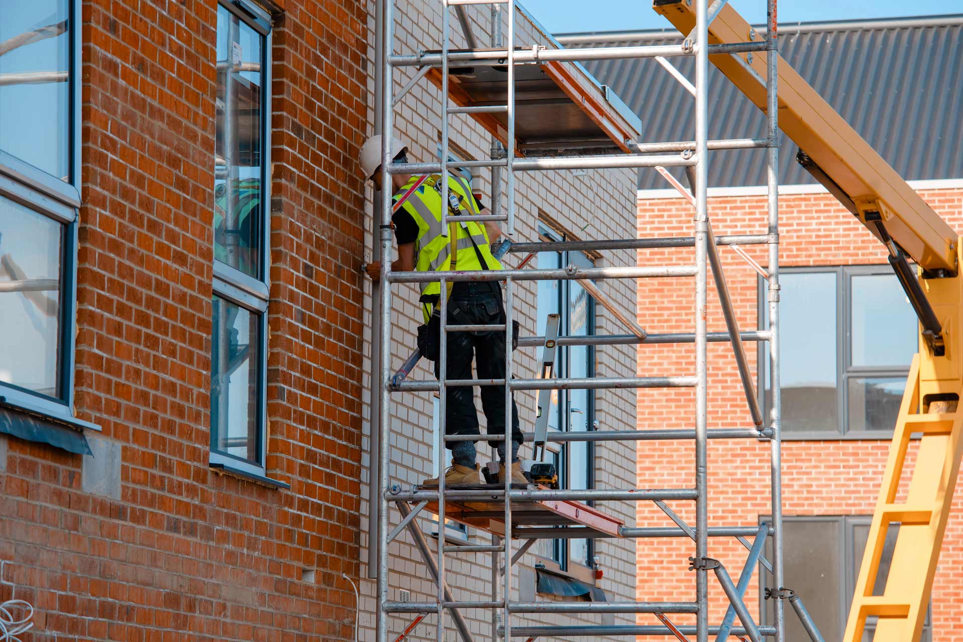 Construction workers using aluminum mobile scaffold tower and safety harness to work at height.