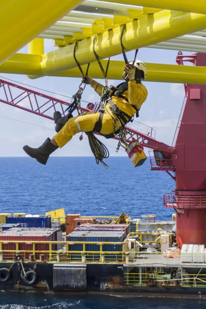 Working at height. Working overboard. A commercial abseiler with fall arrestor device hanging on bridge pipeline structure at oil and gas platform to perform painting works.