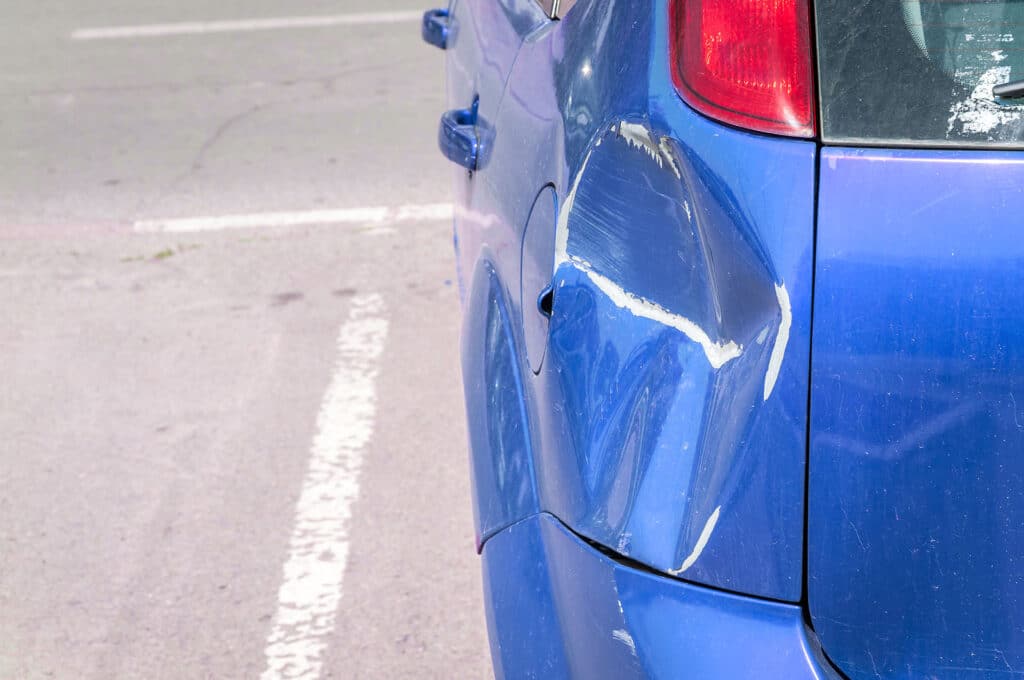 Blue scratched car with damaged paint in crash accident or parking lot and dented damage of metal body from collision