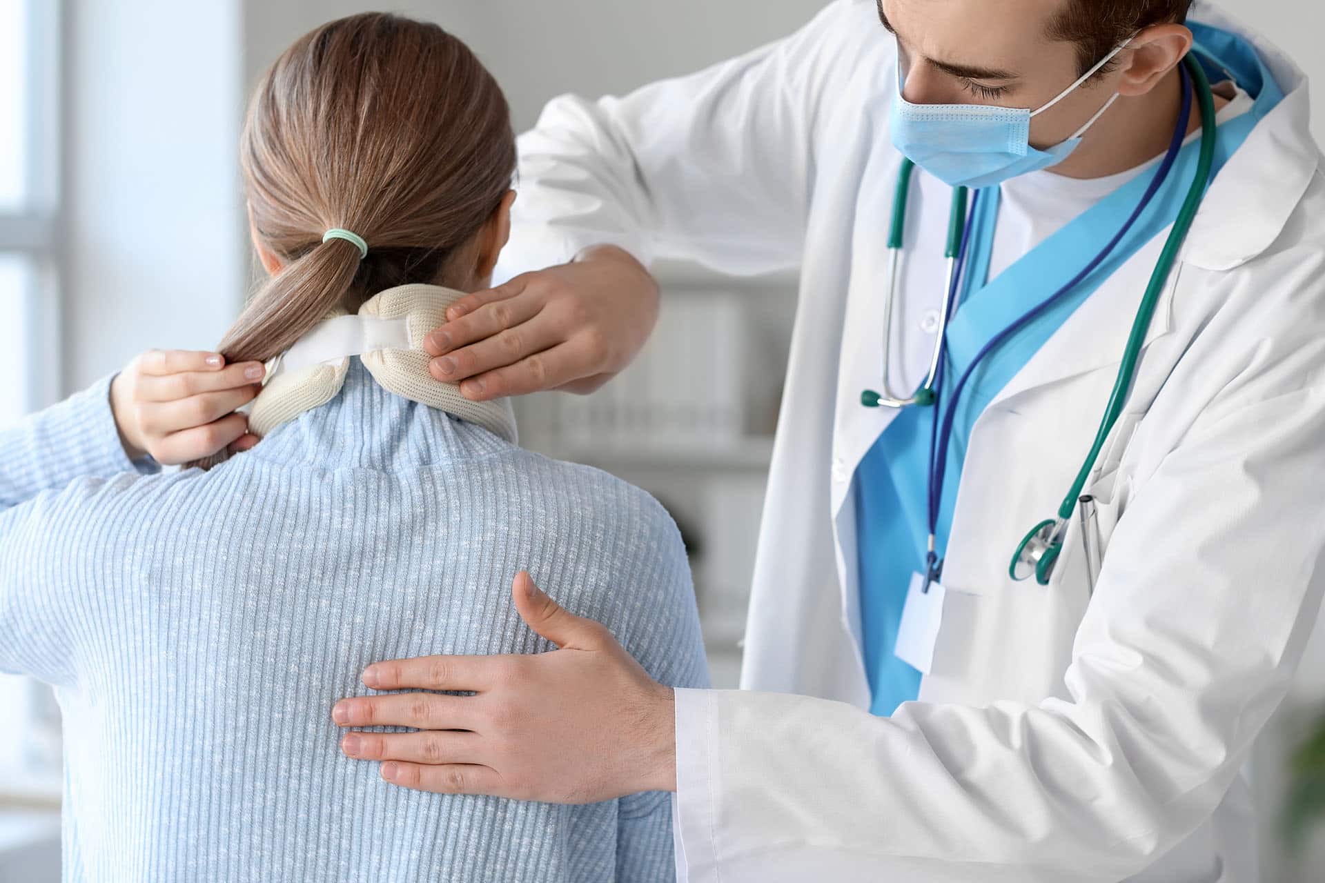 Doctor applying cervical collar on neck of young woman in clinic