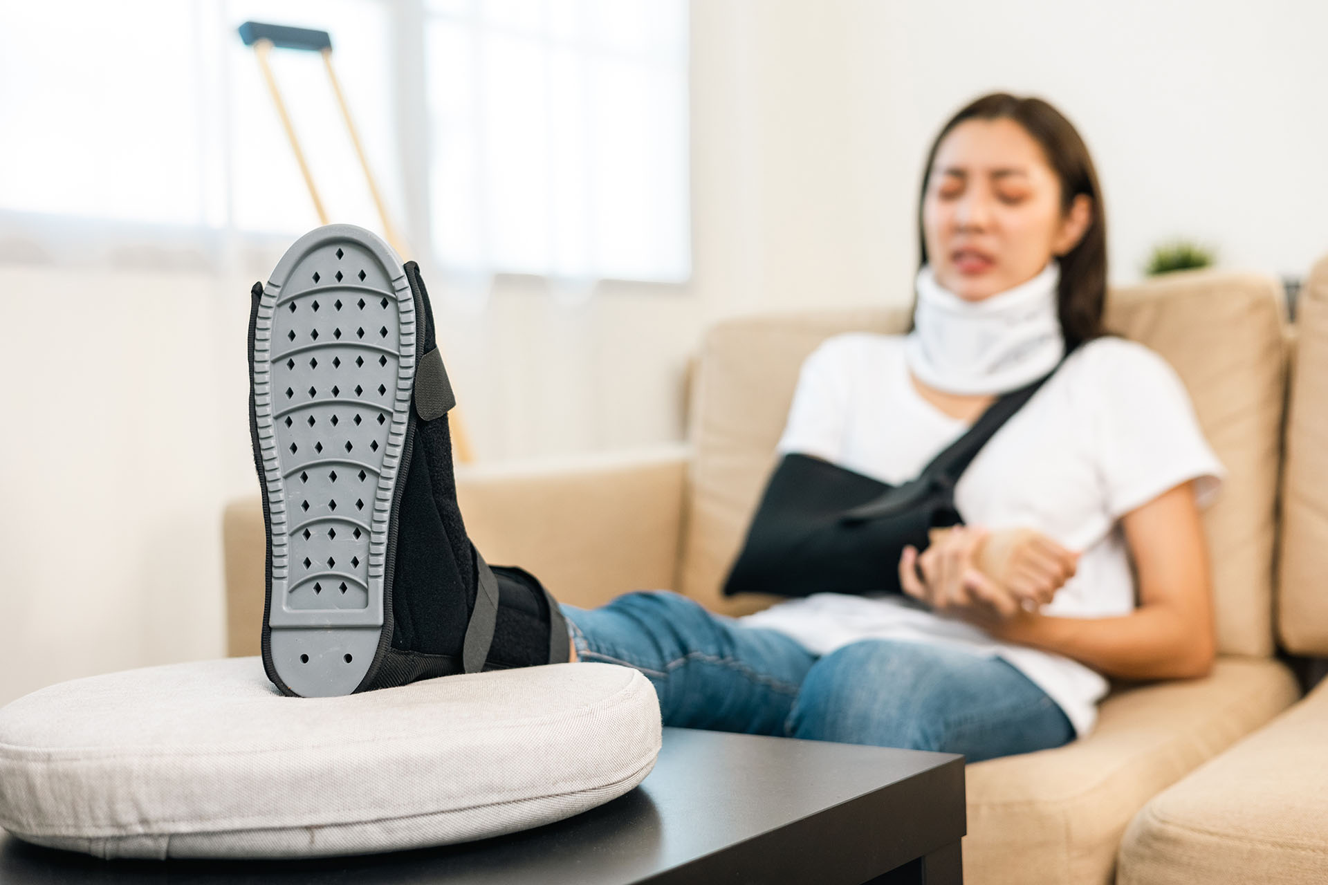 Woman suffered pain from accident fracture broken bone injury with leg splints in cast neck splints collar arm splints sling support arm in living room.