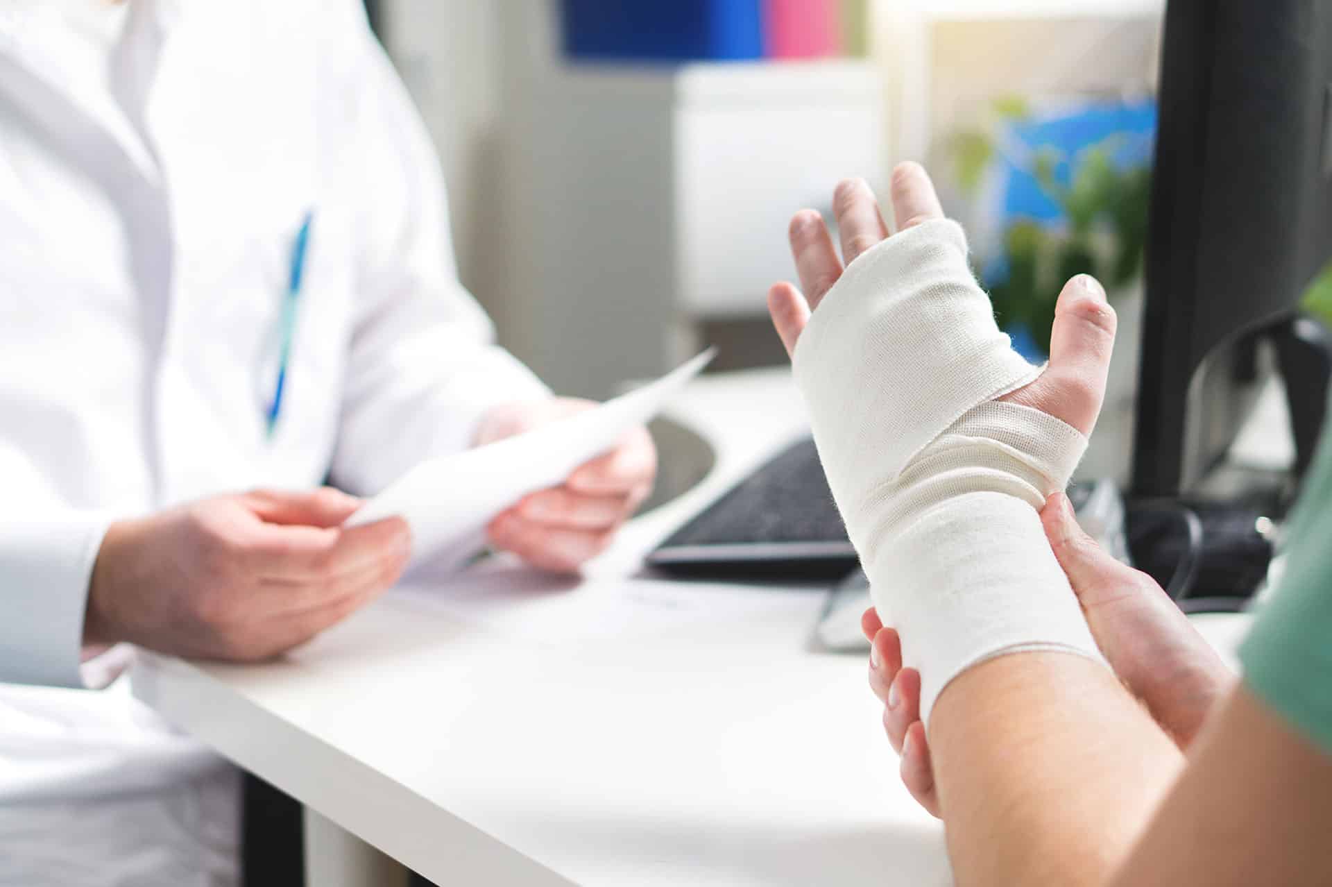 Injured patient showing doctor broken wrist and arm with bandage in hospital office or emergency room.