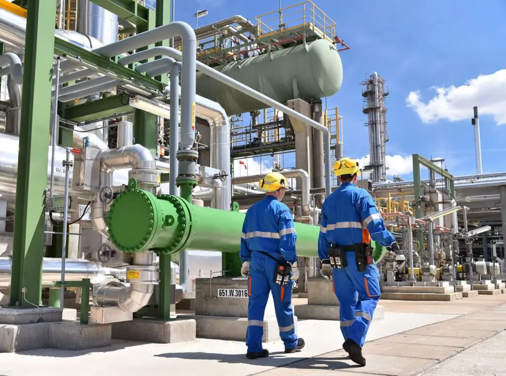 Workers in work clothes in a refinery with pipes and machinery