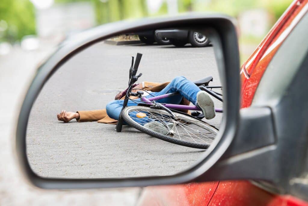 Unconscious male cyclist lying on street after road accident scene through side car mirror