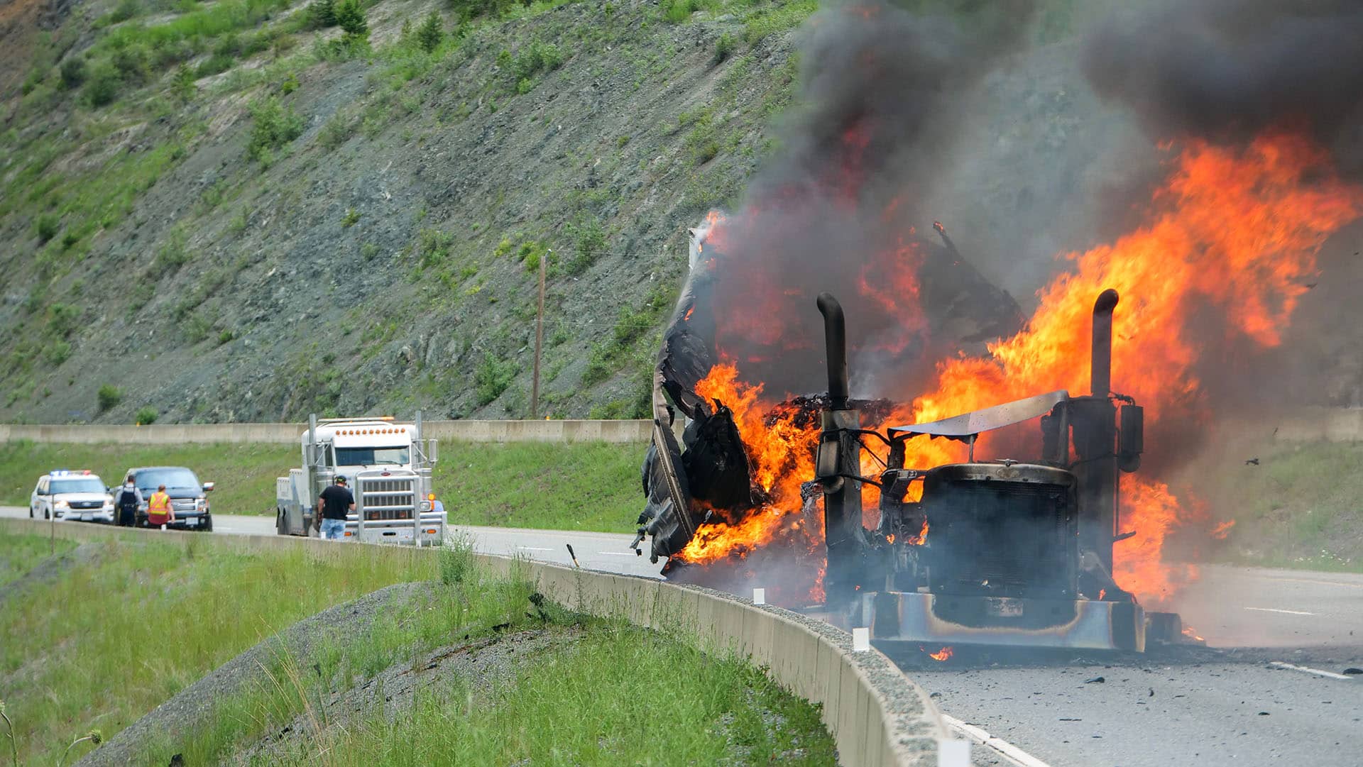 A semi truck burns on the side of the highway