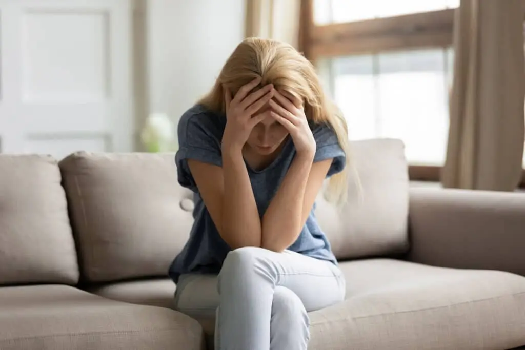 Upset young woman sit on couch at home suffer from depression or mental psychological problems