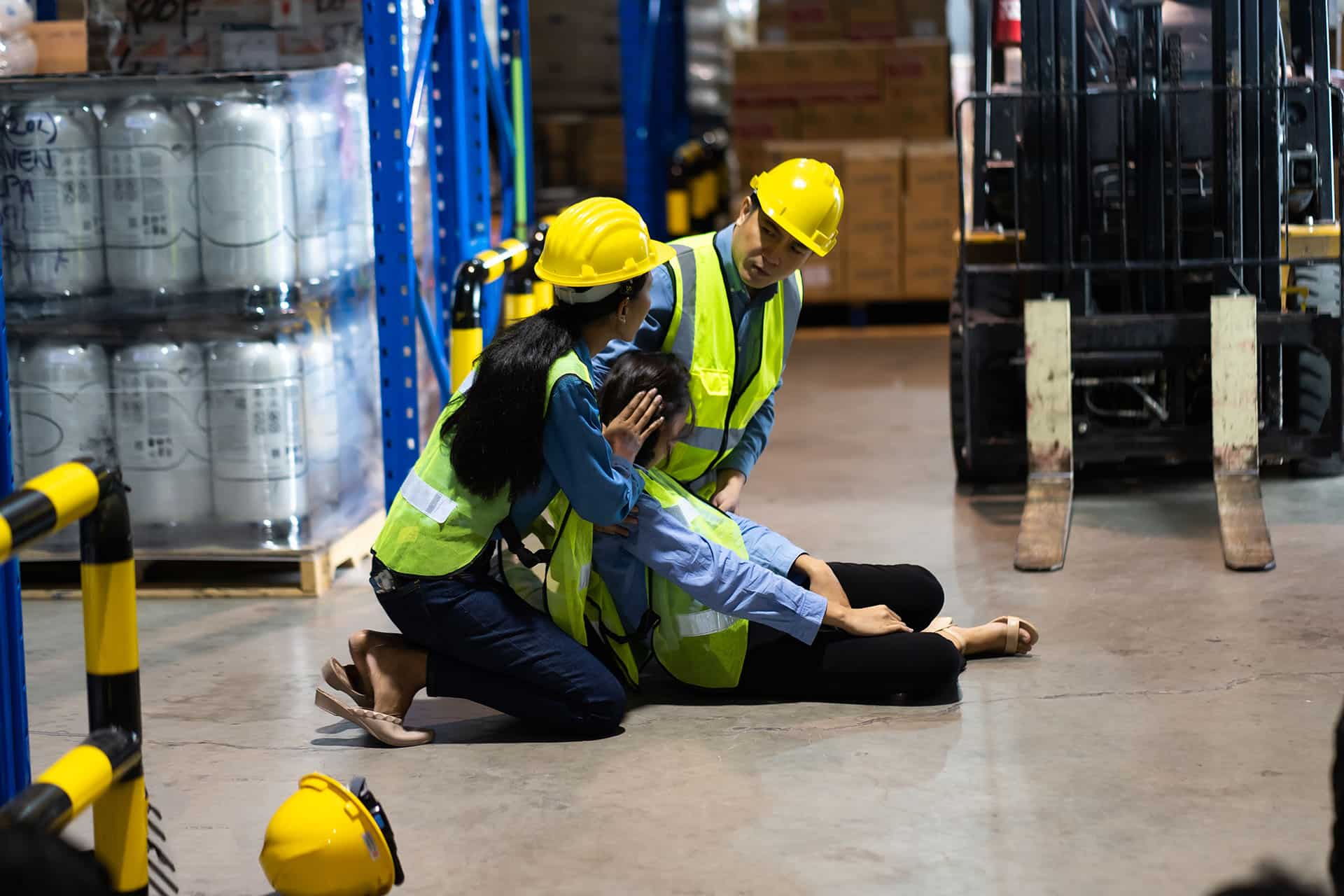 Workers man and woman taking care female colleague lying on the floor in a warehouse.