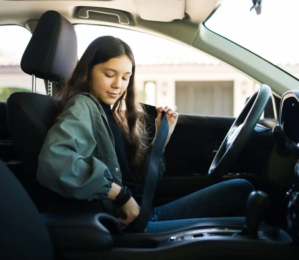 Teenage girl putting on her safety seatbelt and about to start the car.