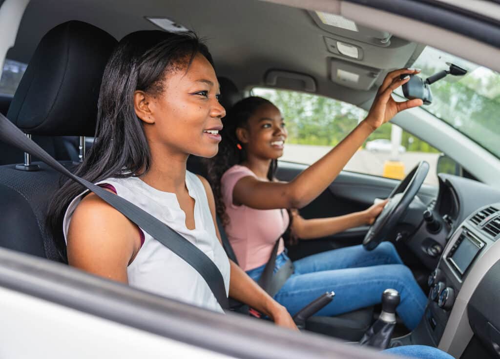 A young black teenage driver seated in her new car with her mother