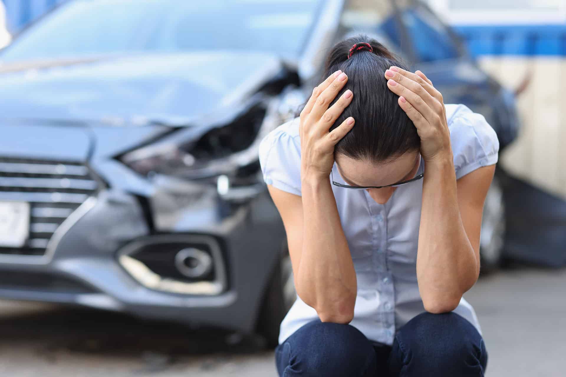 Frightened woman sits in front of wrecked car closeup