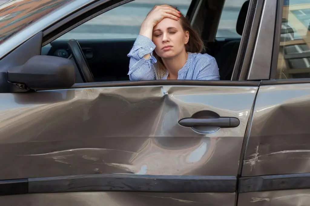 Drunk or injured woman sitting in smashed automobile with closed eyes and palm on forehead