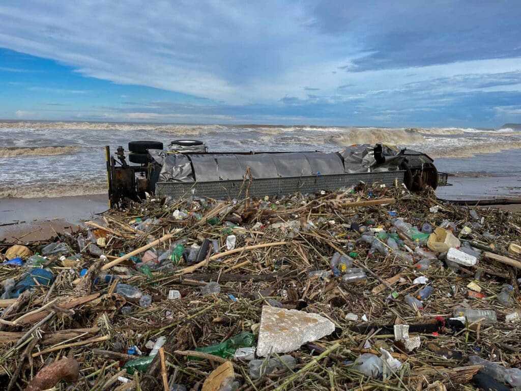 Medium shot of a truck that has washed up on the beach with rubbish and plastic bottles