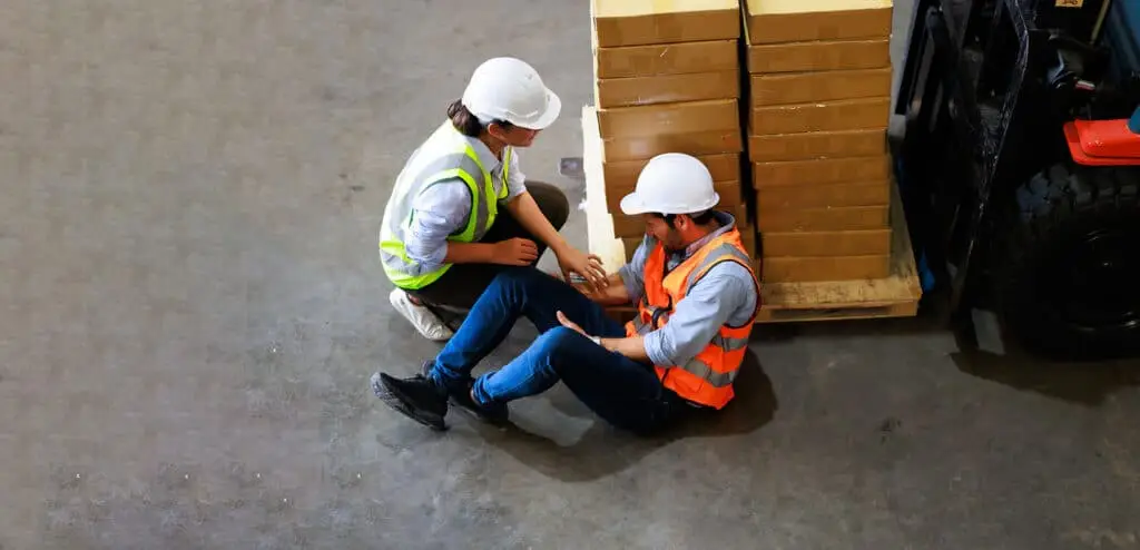 Engineering talking on walki talki radio to employee while his warehouse coworker lying unconscious at industrial factory.