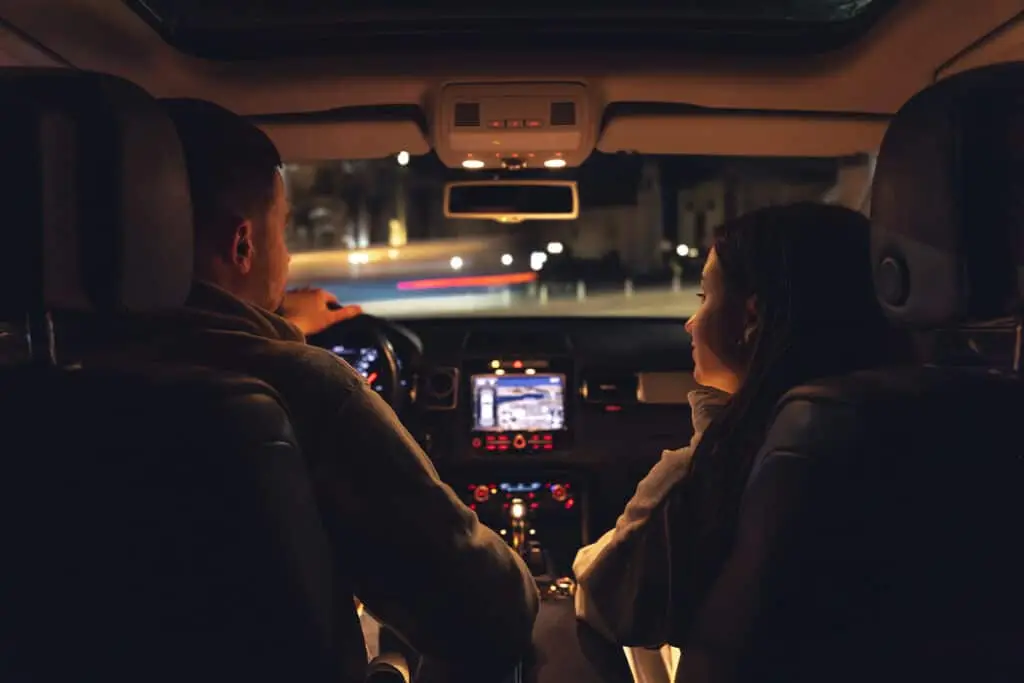 A man and a woman are driving in a car at night, the view from the car to the road.