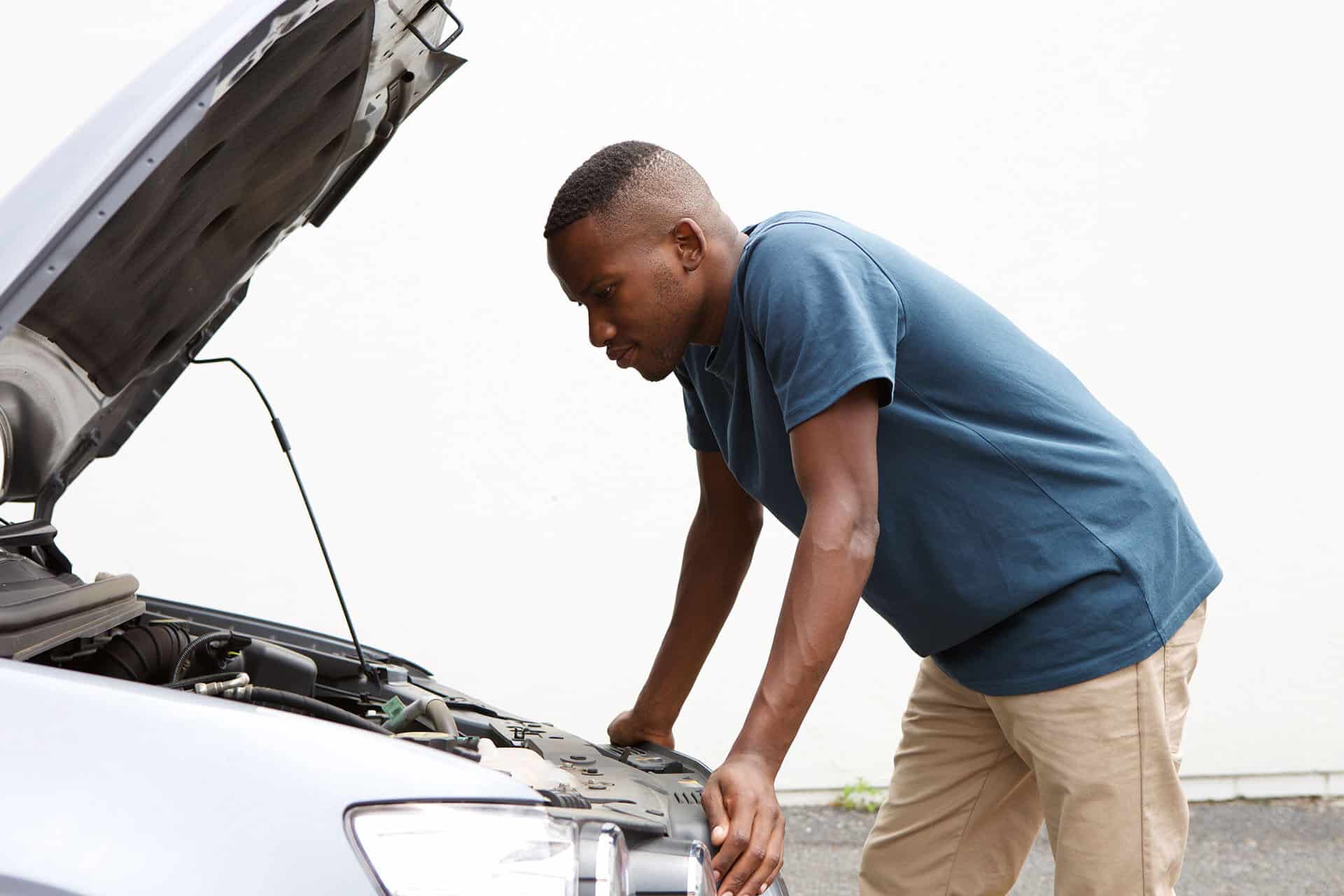 Side portrait of young african man looking under the hood of car