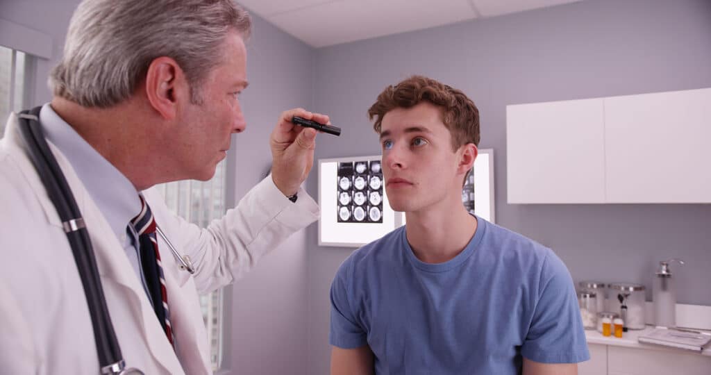 Mid-aged doctor examining eyes of young adult male patient.