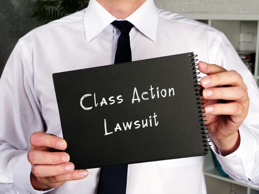 a man in a white shirt with a black tie holding a sign reading class action lawsuit