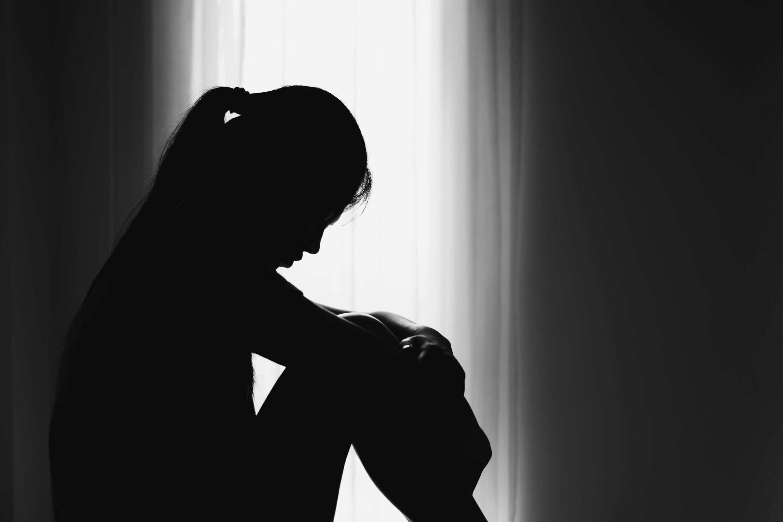 silhouette of a woman sitting against a window symbolizing the trauma of sexual abuse