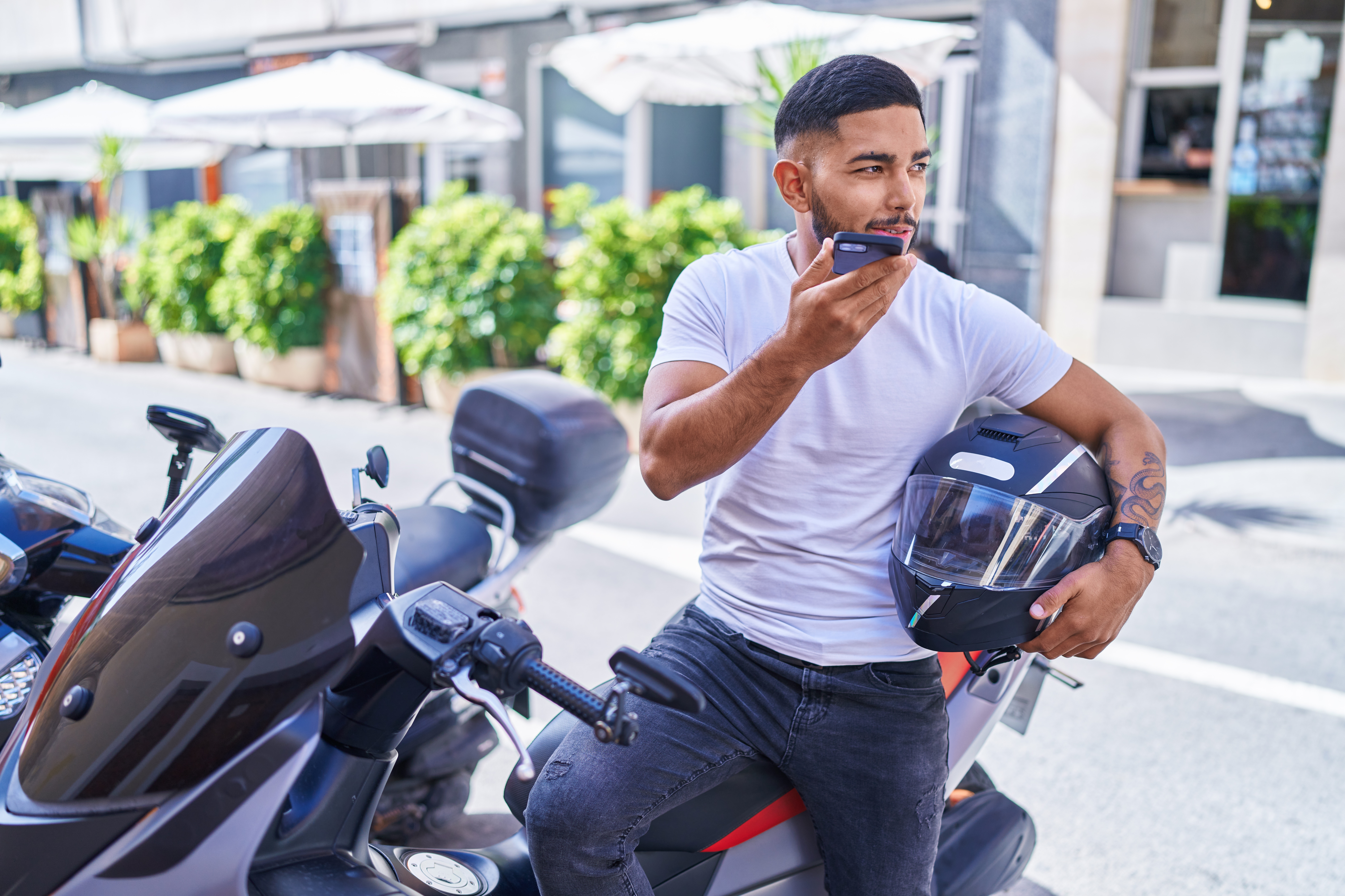 young man holding a helmet and talking on his phone, sitting on his motorcycle
