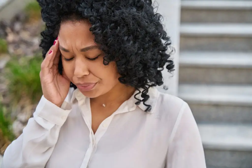 african american woman wearing a white blouse rubbing her temple from a persistent headache after an accident