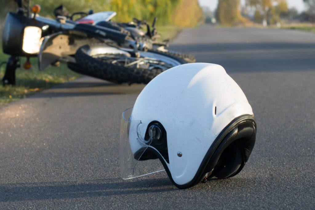 photo of a white motorcycle helmet laying on a paved road after an accident