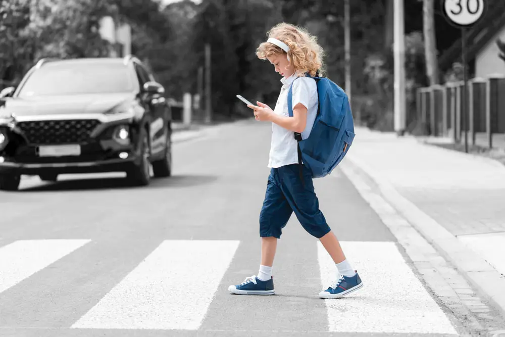 Adorable boy with a backpack, headphones and cellphone goes through the pedestrian crossing