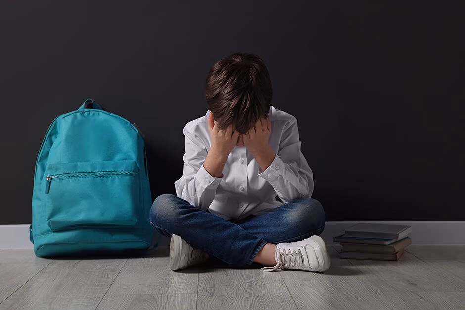 Upset boy with backpack sitting on floor